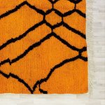 Corner detail of authentic Moroccan rug displaying geometric pattern in orange shades with natural white fringe
