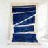 Navy blue Moroccan Beni rug with geometric pattern and cream wool fringe hung against white wall