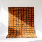 Handwoven Moroccan trellis rug with orange and brown grid pattern on white background