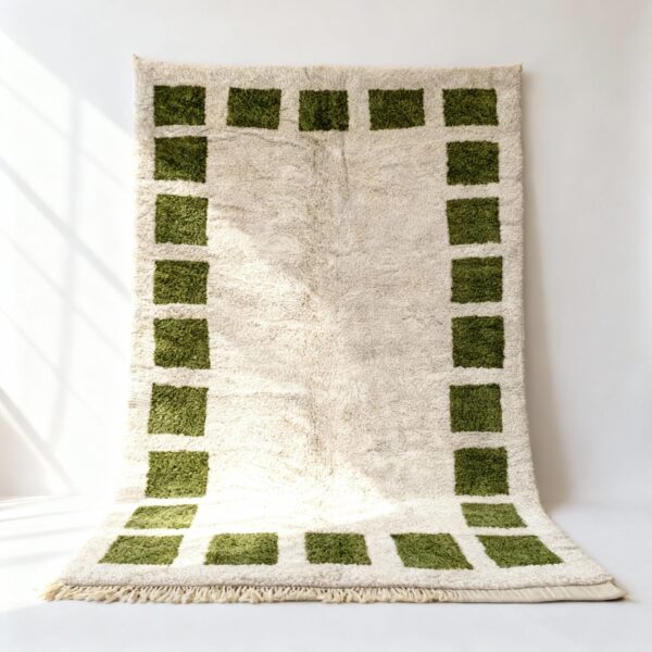 Handwoven Moroccan rug with emerald green square border pattern on cream wool, displayed draped showing plush texture