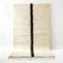 Handwoven cream wool Beni Ourain rug with minimalist single black line design, displayed on white wall