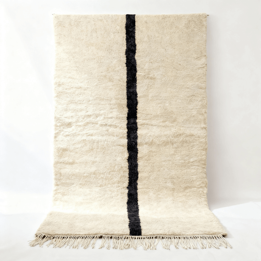 Handwoven traditional Moroccan rug with black single line on ivory wool Traditional Moroccan rug handwoven in cream wool with bold black vertical stripe, featuring plush Beni Ourain style