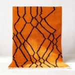 Handwoven Moroccan rug with vibrant orange wool and bold black geometric diamond pattern with white fringe trim