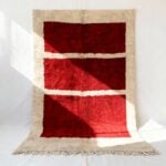Red handwoven Moroccan area rug with three horizontal cream stripes on beige border, minimalist grid design