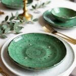 Handcrafted Tamegroute pottery plates in emerald green on white dinnerware with gold flatware and eucalyptus