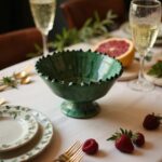Green ceramic pottery bowl on elegant dining table with champagne glasses and fresh grapefruit