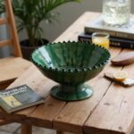 Traditional green ceramic pottery bowl on rustic wooden table with books and orange juice
