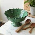 Moroccan green ceramic pottery bowl with wooden spoons on white marble countertop