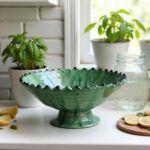 Green ceramic pottery bowl centerpiece on farmhouse table with eucalyptus leaves and white plates