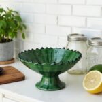 Handcrafted green ceramic pottery bowl with decorative ruffled edge on formal dining table setting