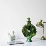 Green ceramic candlestick with sunburst design displayed on marble surface with decorative items and desk lamp