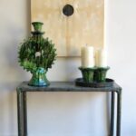 Tamegroute green ceramic candlestick with spiky sunburst pattern next to cream candles on rustic console table