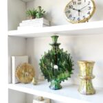 Handcrafted green ceramic candlestick with sunburst design on white shelf next to yellow matching vase and clock
