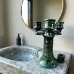 Green ceramic candlestick holder styled on marble surface near mirror, showing triple arm design and craftsmanship