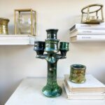 Green glazed ceramic candlestick holder with three arms on bookshelf styling with vintage books and accessories