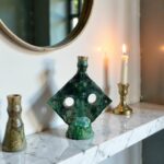 Close-up of green ceramic candlestick with drip glaze patina on marble surface beside lit candle