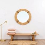 Natural straw round mirror with compact woven frame above wooden bench in serene minimalist boho interior