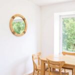 Handwoven raffia round mirror in light-filled dining room with natural wood furniture and minimalist bohemian style