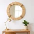 Round natural straw mirror with tight woven frame above wooden desk with brass lamp and plant in bohemian office