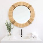 Handwoven boho round mirror with straw frame above white bathroom vanity sink creating organic spa decor