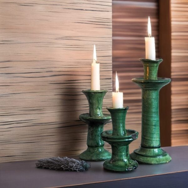 Set of green ceramic clay candle holders with crackle glaze and lit white candles on dark surface