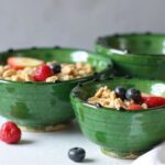 Close-up of green ceramic clay bowl with breakfast cereal, highlighting natural glaze and scalloped rim detail