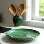 Single Tamegroute pottery plate in glossy emerald green glaze showing handcrafted ceramic texture near kitchen window