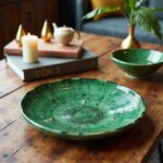Artisan Tamegroute pottery plates with rustic green glaze and amber rim accent on wooden table with candles