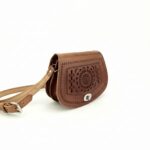 Angled side view of embossed leather mandala crossbody bag showing structured saddle shape with gusset and adjustable strap