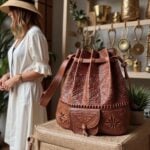 Brown leather backpack with hand-tooled floral and geometric patterns displayed on wicker chair in interior setting
