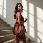 Convertible leather backpack worn as shoulder bag against stucco wall with palm shadows, showing hand-tooled motifs
