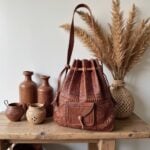 Hand-tooled brown leather backpack with embossed floral motifs displayed alongside pottery and dried botanicals