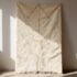 Hand-knotted Beni Ourain wool rug with diamond pattern and fringe, hanging in studio