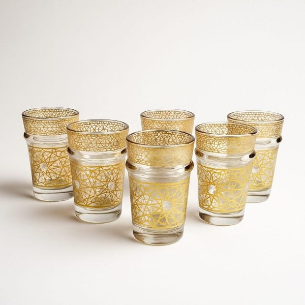 Close-up of six handmade gold Moroccan tea glasses with an intricate golden lattice pattern, photographed on a clean white backdrop.