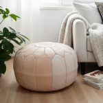 Natural leather floor ottoman in modern living room with white sofa, knit throw blanket, and indoor plant on wood floor