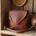 Brown leather crossbody purse showing envelope flap detail and brass zipper on wooden shelf