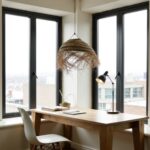 Handwoven straw lighting fixture with natural fibers near corner windows in modern home office workspace