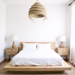 Straw chandelier providing warm light above neutral bedroom with wooden accents