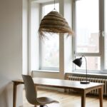 Artisan handwoven straw chandelier suspended above white bedding with natural wood nightstands creating serene atmosphere