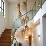 Cascading handwoven straw pendant lights with fringe illuminated in modern stairwell with glass railing