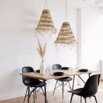Pair of straw pendant lamps hanging above modern dining table with black chairs