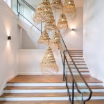 Cascading straw pendant lamps illuminating modern staircase with glass railing