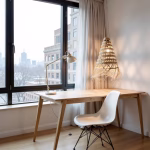 Handwoven straw pendant lamp above wooden desk near city window