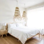Two handwoven straw pendant lights with cascading fringe hanging over bed in bright white bedroom