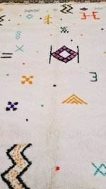 Close-up of boho rug showing hand-knotted geometric symbols in orange, black, and teal on natural wool texture