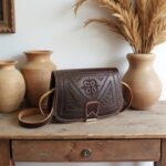 Brown embossed leather shoulder bag styled with pottery on rustic wooden console with natural decor
