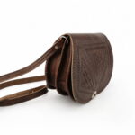 Side profile of embossed leather saddle bag showing geometric border and saddle stitching