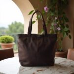 Dark brown leather tote bag with center seam detail on marble surface near archway