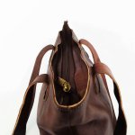 Leather tote bag handles close-up showing reinforced attachment and brass zipper pull