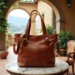Handcrafted leather tote bag in cognac brown on marble table with Italian courtyard backdrop